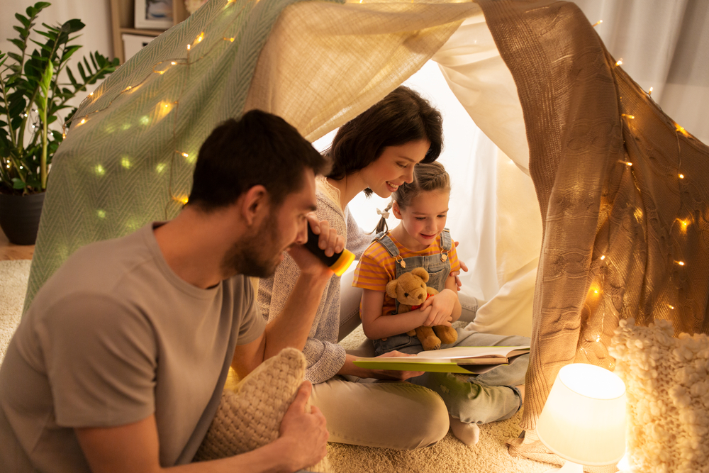 Family sitting in an indoor DIY tent with lights reading a book - Family Christmas Gifts - The Grandkid Connection