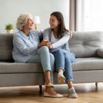 Granddaughter and teenage granddaughter sitting on couch together smiling at one another - Long-distance teenage grandchildren - The Grandkid Connection